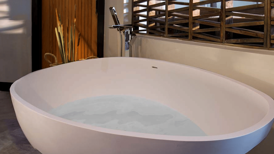 A bathroom at Tamarind Hills Resort and Villas, Antigua, featuring a large freestanding oval bathtub, a faucet, and wooden accents.