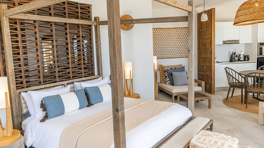 A king bed with beddings, in a canopy, pendant lights, a table and chairs at Tamarind Hills Resort and Villas, Antigua.