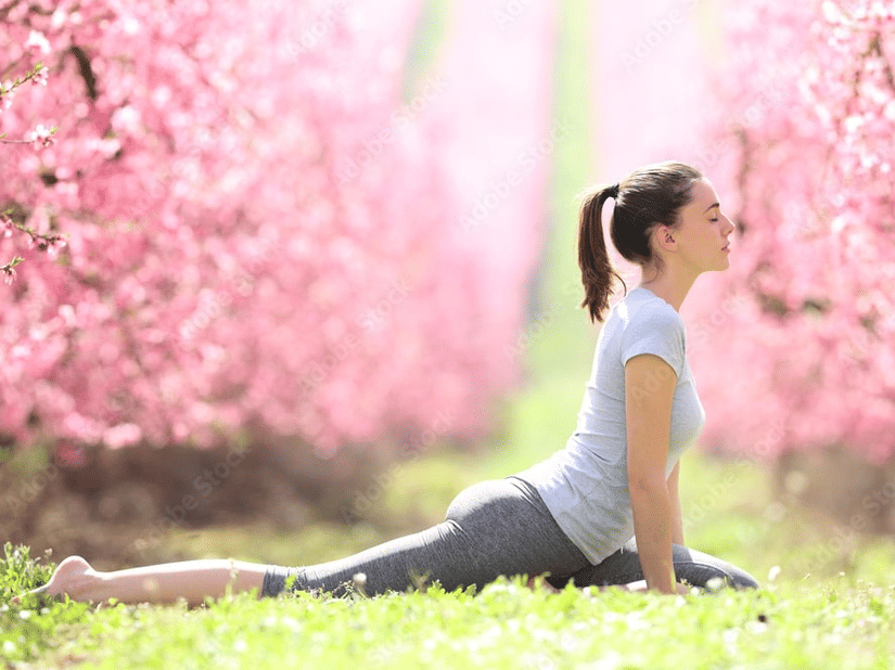  A woman in yoga pants is performing a yoga pose in a blossoming pink orchard.