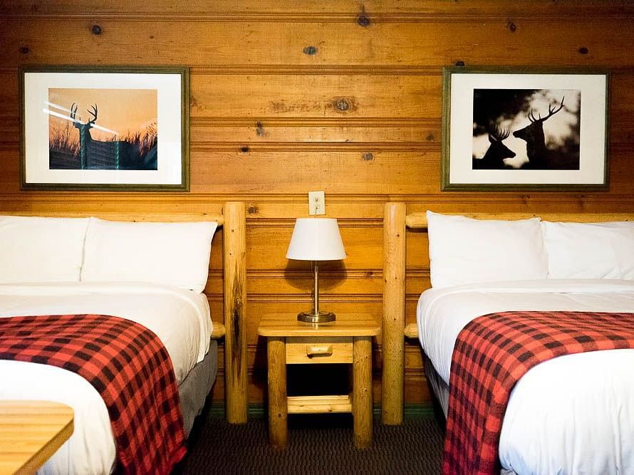 A wooden cabin with twin beds and a side table with a night lamp placed between them at Shaver Lake Village Hotel.