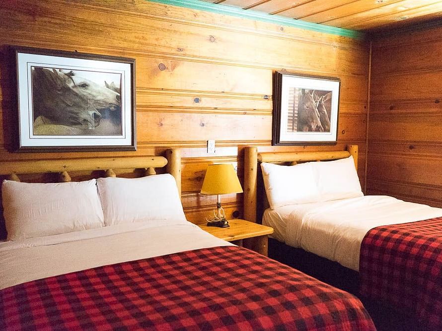 A wooden cabin with twin beds with photographs hung on the wall behind them at Shaver Lake Village Hotel.