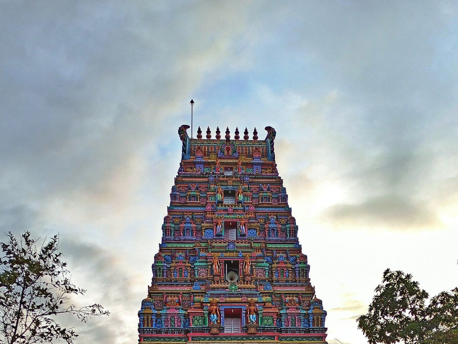 A large, multi-level red temple tower with a long, paved walkway leading to it under a partly cloudy sky.