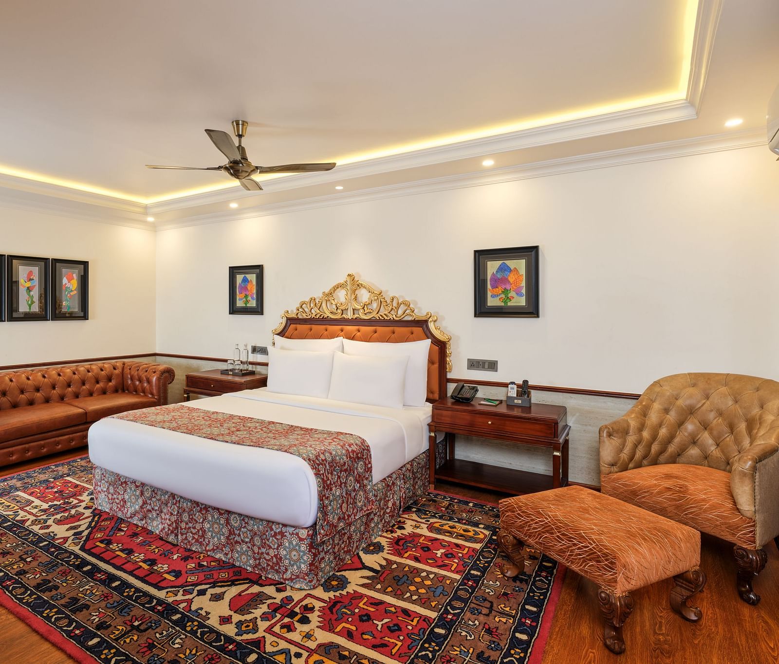 a luxurious Executive Suite with a large bed on a decorative rug, sofas, tables, artworks on white walls