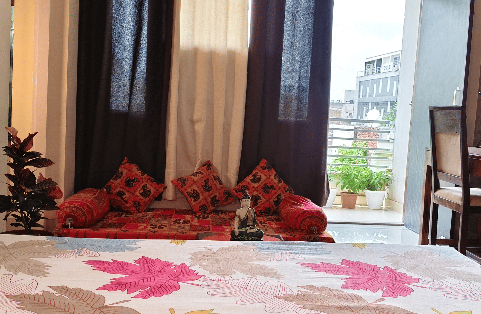 A well-lit bedroom with a large bed, patterned bedding, window curtains and chairs near the balcony at Jaypore360 Homestay - Best Homestays in Jaipur.