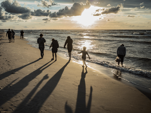  A family walking along a sandy beach at sunset, casting long shadows on the ground next to ocean waves.