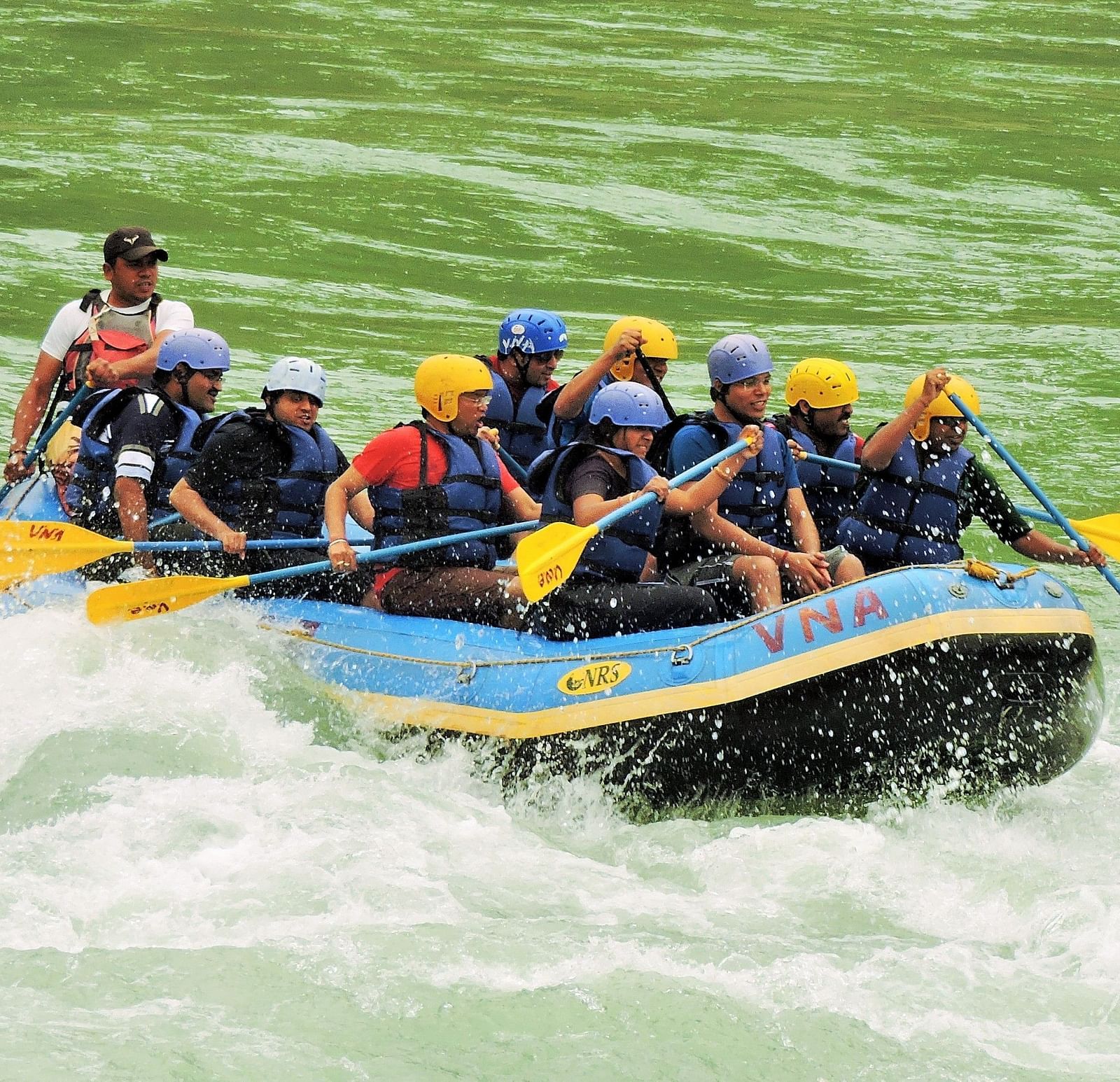 A group of people rafting on a single raft in a rushing river, splashing water around them. 
