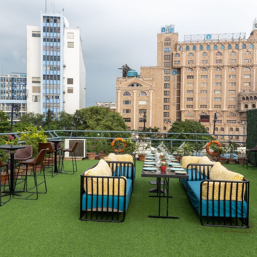 A rooftop garden cafe with artificial grass, potted plants, and a view of an ornate building in the background. - Polo Floatel, Kolkata