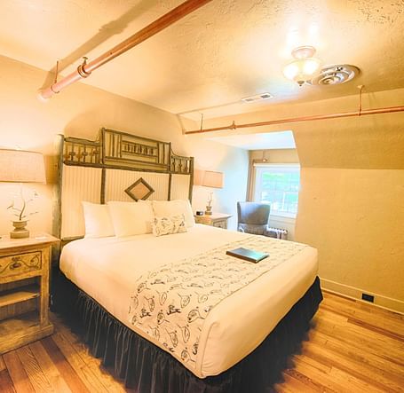 a comfortable double bed with a huge head board behind it in a warmly illuminated room - Historic Tapoco Lodge