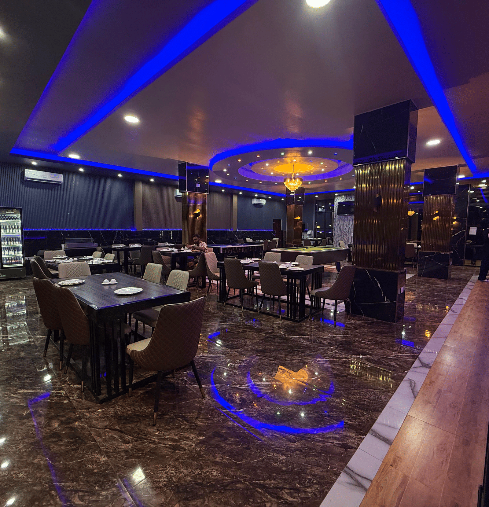 A panoramic view of a restaurant or bar interior, featuring dark decor, shimmering floors, and vibrant blue neon strip lighting at Luffu Club.