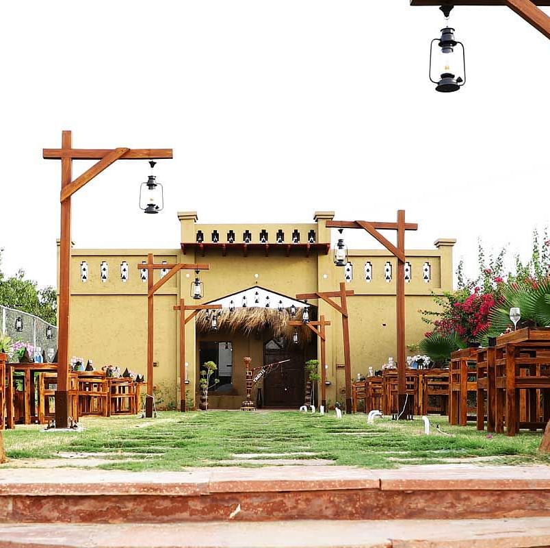 An image of lawn which has tables and chairs placed beyond that there is a single storey building - Themis Barbecue House