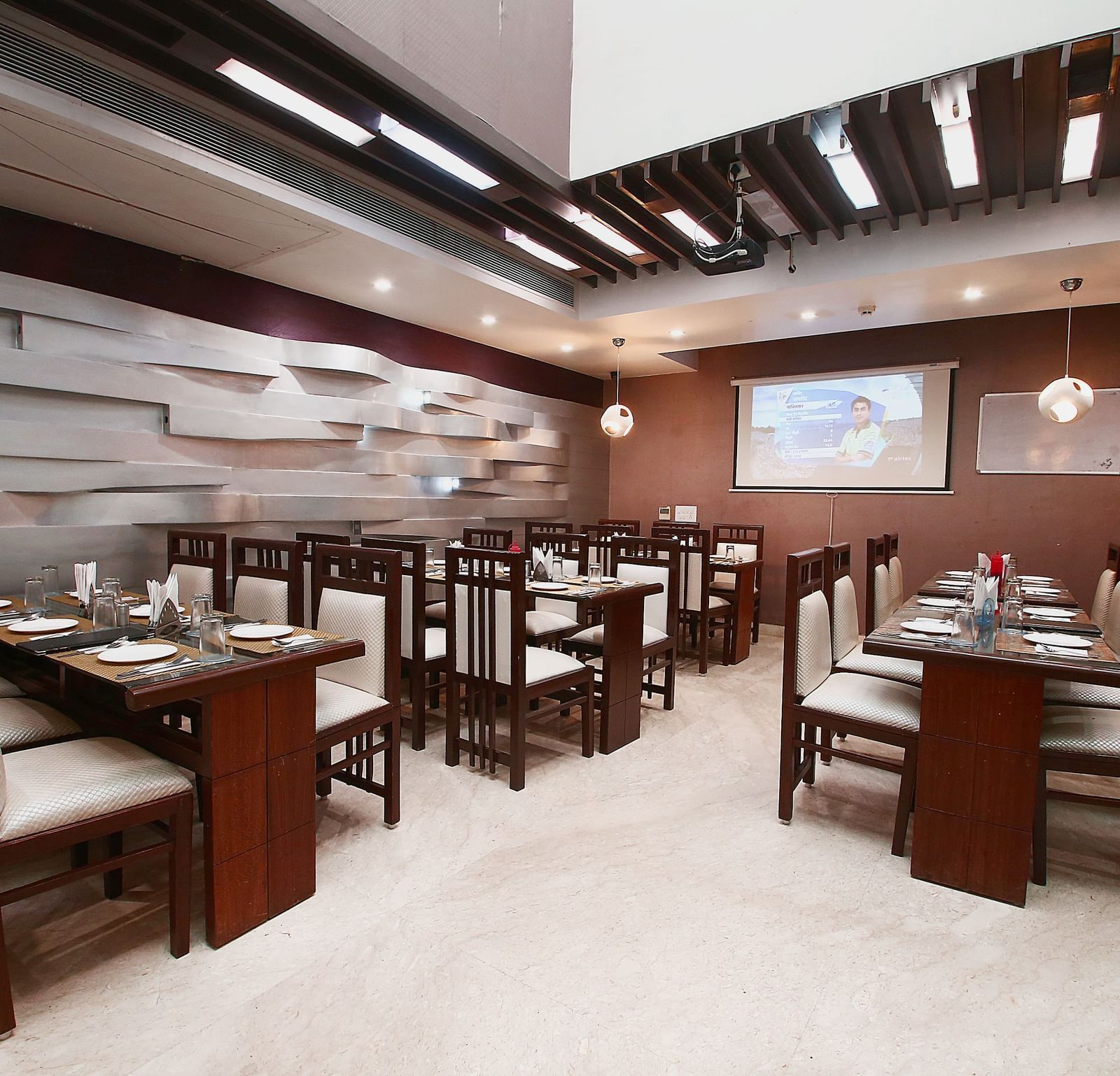 Modern dining space with various tables and chairs for guests to sit in and dine along with beautiful textured patterns on the wall and ambient  lighting - Hotel Emerald, Chandigarh