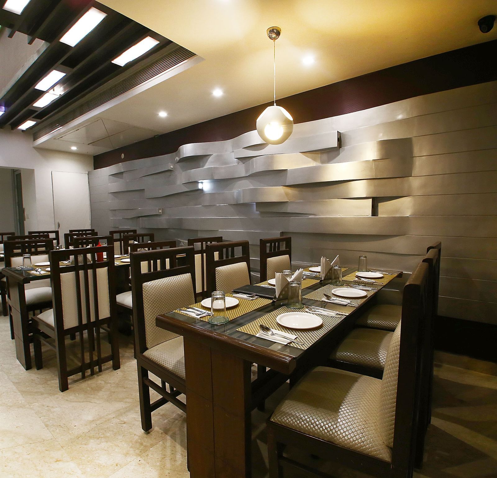 Uniformly placed chairs and tables of mocha and dark shades  in a modern light setting an extremely detailed walls and interior - Hotel Emerald, Chandigarh