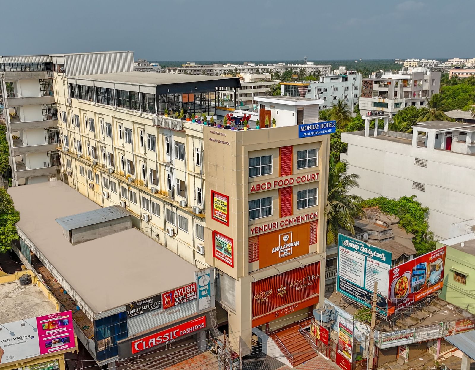 Aerial view of Monday Hotels Amalapuram Heights surrounded by other buildings and trees.
