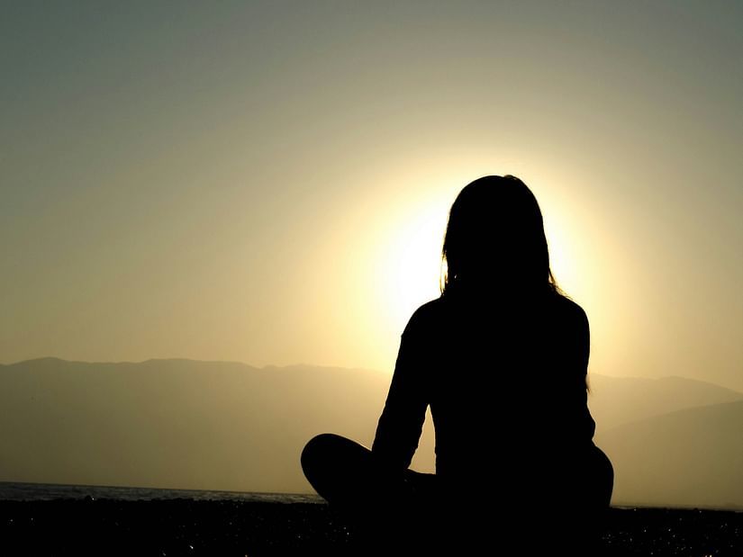 A silhouette of a girl in a meditation pose with the sun in front of her.