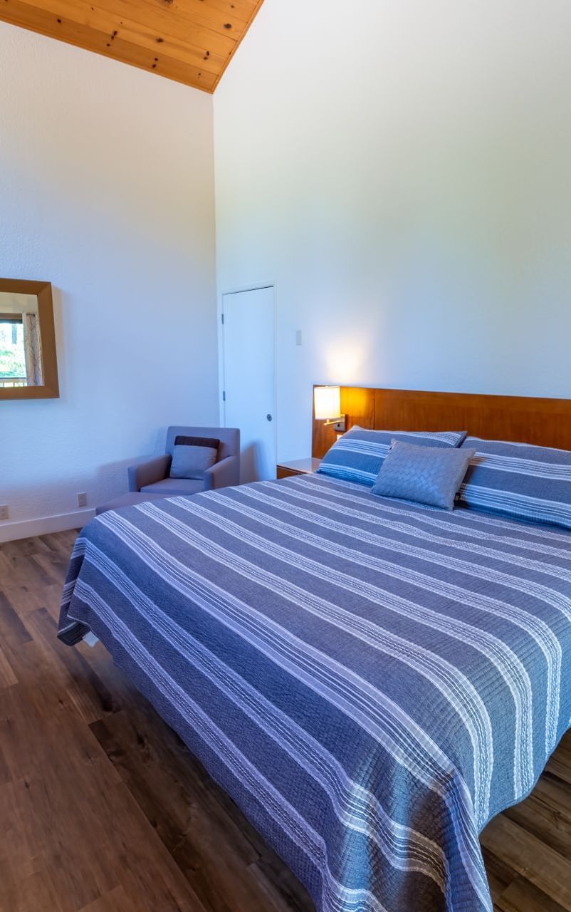Deluxe King Room at Amador Hotel with a king-sized bed, wooden flooring, wall lamps, and a mirror above a dresser.