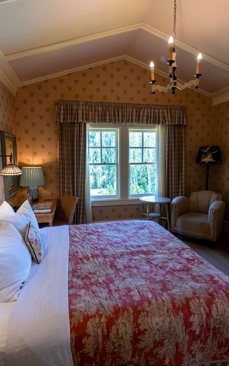 Side view of a room in Tallman Hotel, featuring plush bedding, an arched ceiling, an upholstered sofa for one, and ample natural lighting entering from the open glass windows.