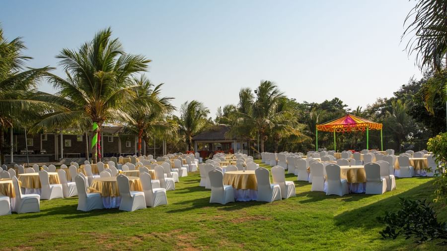An expansive outdoor event setup on a large green lawn with many tables and chairs draped in white, under tall palm trees | Grande Pavillion | Grand Bay Resort and Spa