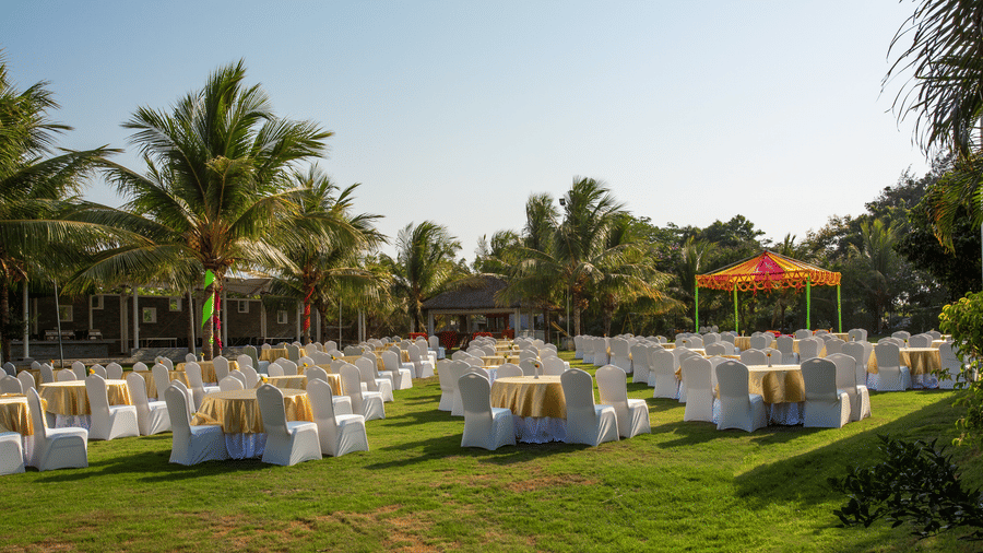 An expansive outdoor event setup on a large green lawn with many tables and chairs draped in white, surrounded by tall palm trees - Grande Bay Resort & Spa, Mamallapuram