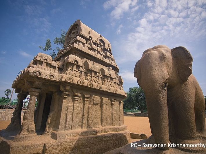 Side shot of a small temple with a huge sculpted elephant on the side and cloudy sky in the background.