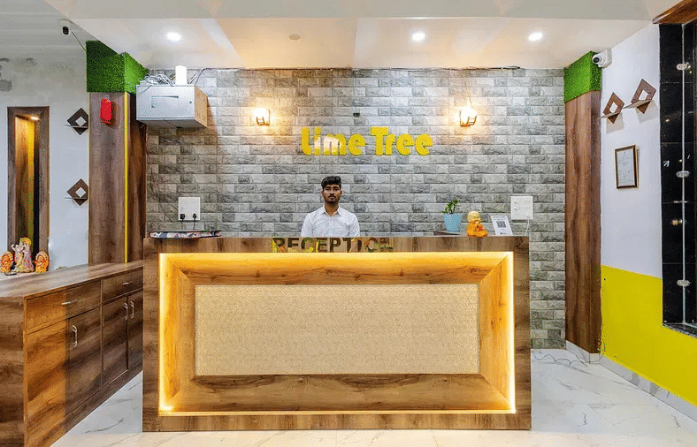 A hotel reception area with a wooden counter, yellow accents, and a stone-textured wall - Lime Tree Hotels & Banquet, Vrindavan