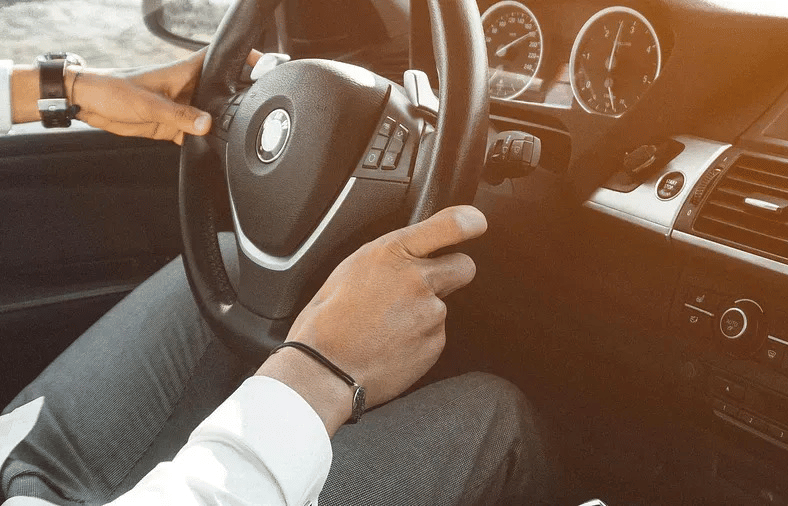 A person driving a car, with a focus on the steering wheel and dashboard.