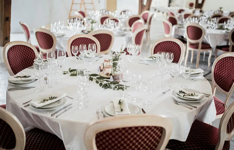 A banquet setup with round tables, white tablecloths, and neatly arranged cutlery and glasses.