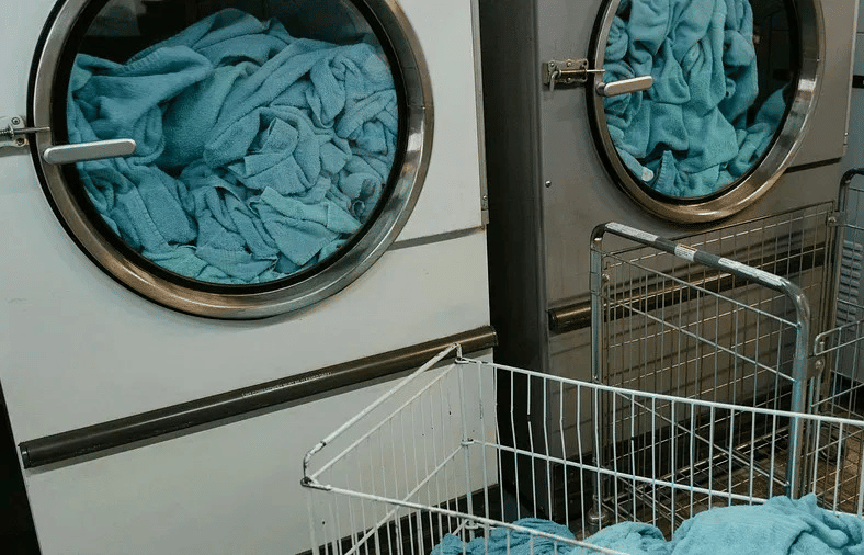 A laundry area with open washing machines and a metal basket filled with blue linen.