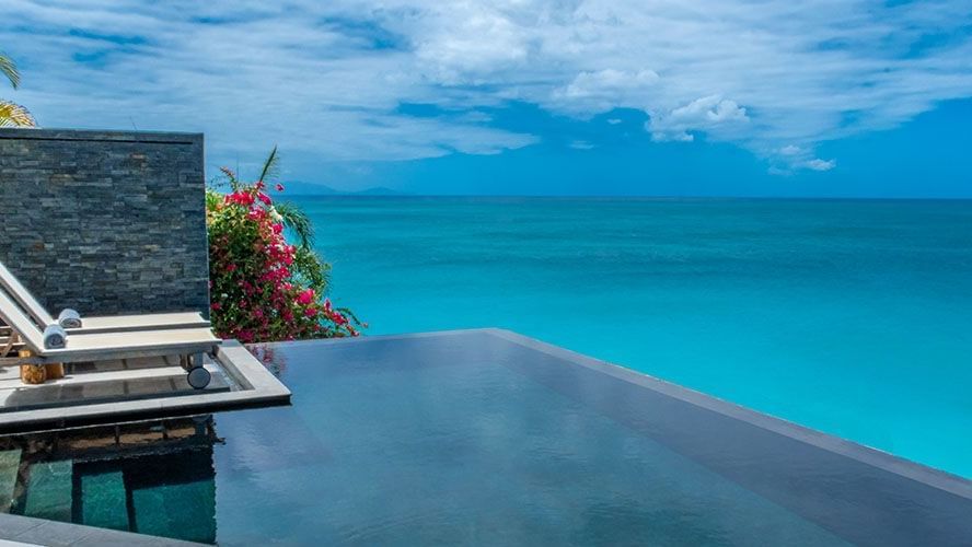  An inviting infinity pool stretches towards the vibrant turquoise ocean under a bright blue sky, with a modern sun lounger nearby - Tamarind Hills Resort and Villas - Antigua