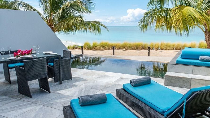 Outdoor lounge and swimming pool of Tamarind Hills Resorts and Villas, Antigua offering the best view of the Caribbean Sea from between trees.