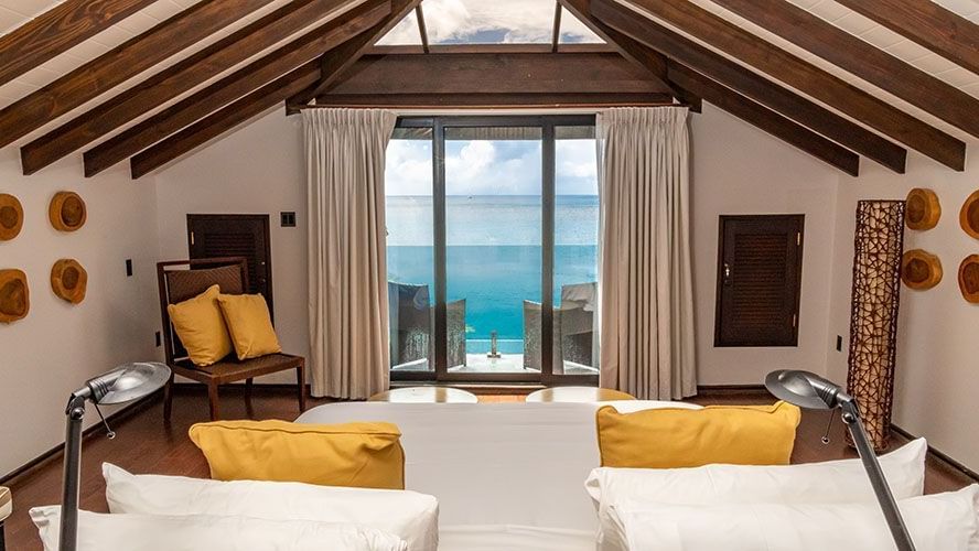 Image of a room a bed and a open balcony overlooking the sea.
