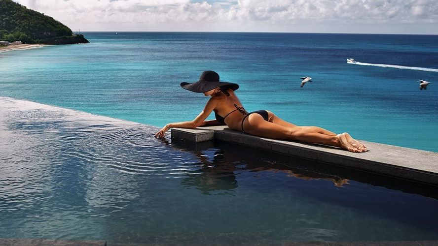  A person lying on the infinity edge pool with a background of the vast Caribbean Sea.