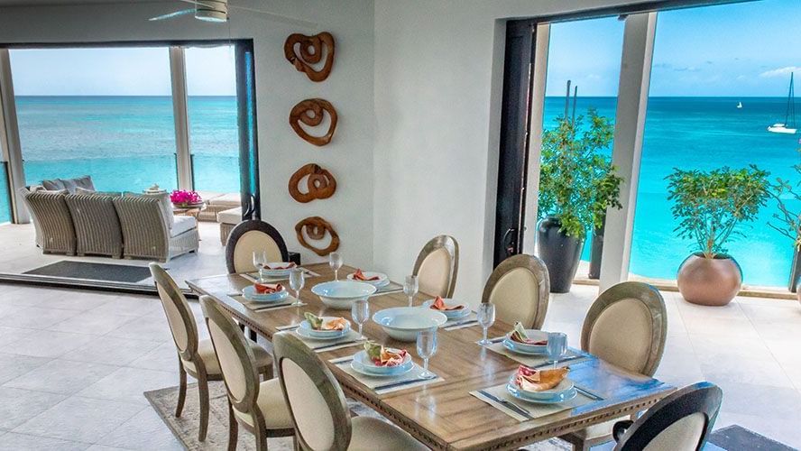 A dining table fully stacked with cutlery in a spacious room that also offers a view of the beach outside.