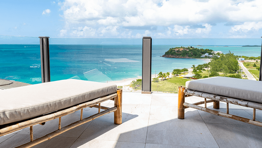A luxurious outdoor lounge area with comfortable seating offers panoramic views of a stunning bay with clear blue water and green islands.