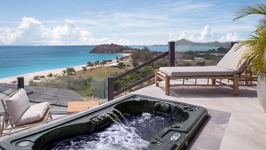 Water pouring into a Jacuzzi placed outdoor alongside a sunlounge offering a stunning view of the Caribbean Sea.