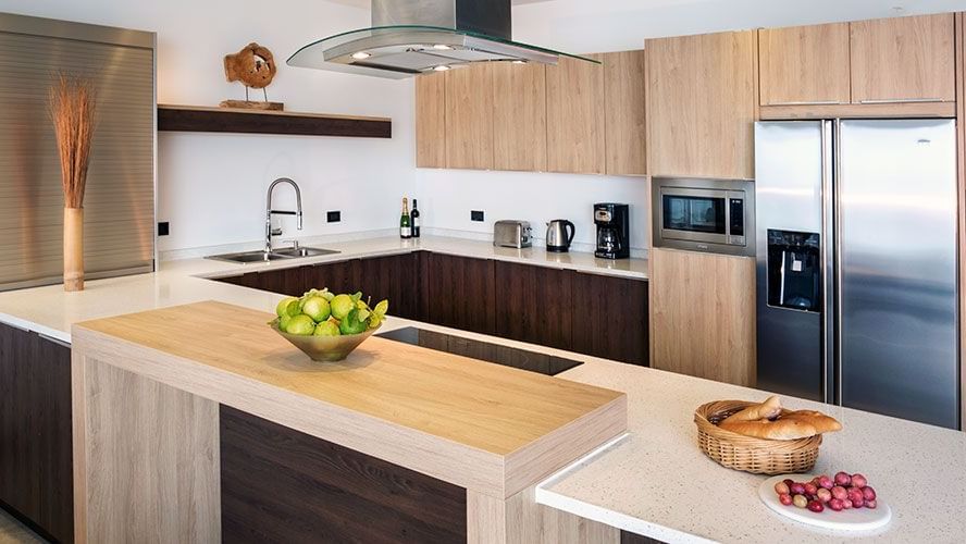 Modern kitchen with wooden cabinetry, sleek appliances, island counter, and bowls of fresh fruits and bread for a cosy touch.