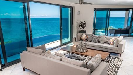 Modern ocean-view living room with floor-to-ceiling windows and luxury seating.