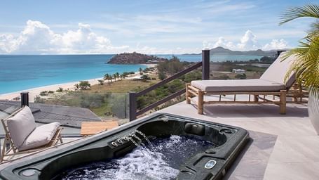 A stunning beachside terrace with a bubbling hot tub, sun loungers, and panoramic ocean views.