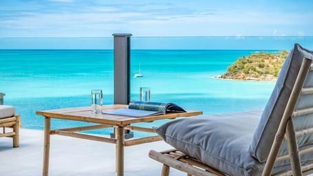 Private terrace with sun loungers and dining set overlooking the turquoise Caribbean Sea and a rocky islet