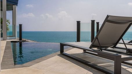 Luxury oceanfront deck with sun loungers beside a private infinity pool at Tamarind Hills Resort and Villas, overlooking the Sea.