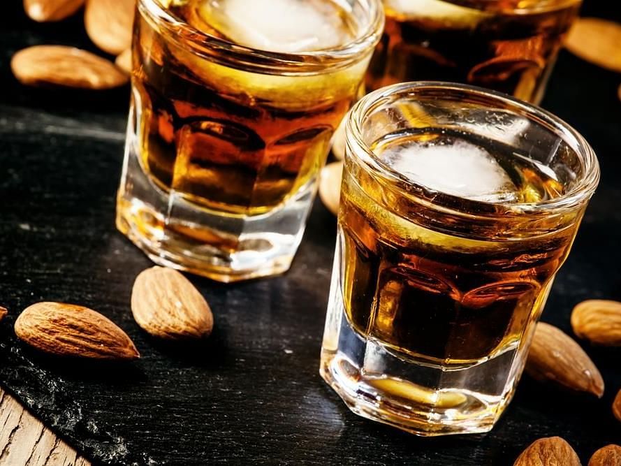 Two glasses of whiskey served with roasted almonds on a rustic surface.