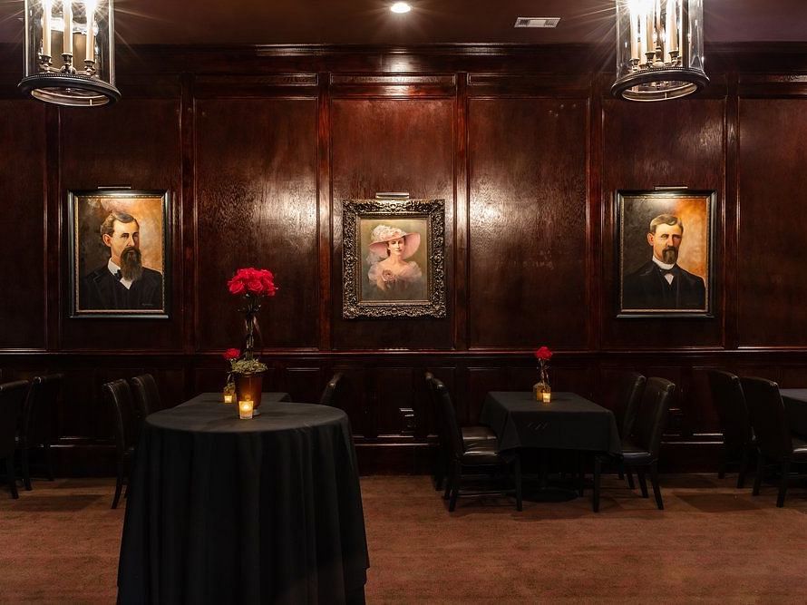 A dimly lit lounge with wooden walls, framed portraits, and intimate seating.- The Grand Hotel & Ballroom, McKinney