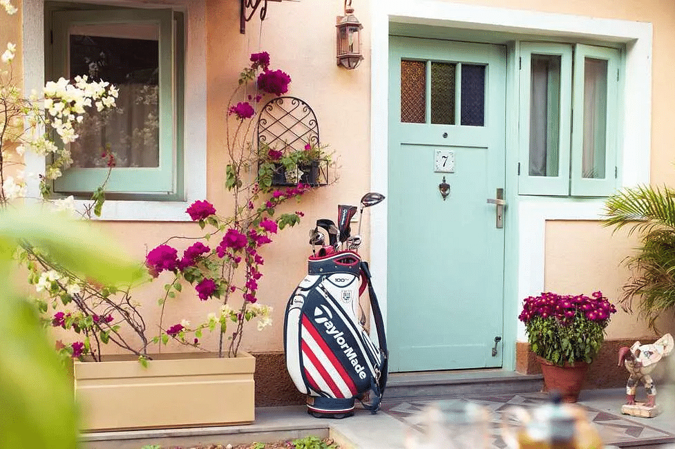 Exterior of Karma Chalets showing a mint green door, flowers in pots, a golf bag, and a wall light next to the entrance.