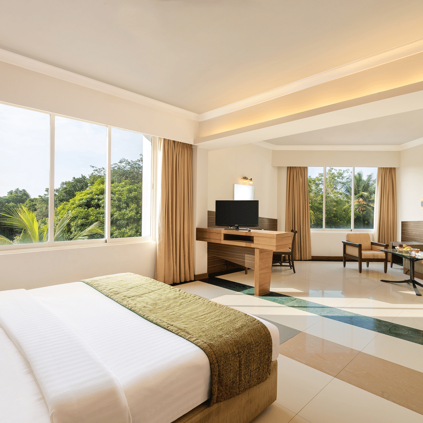 An overview of the Suite with a double bed and a separate living area with a sofa seating arrangement at Sangam Hotel, Thanjavur.