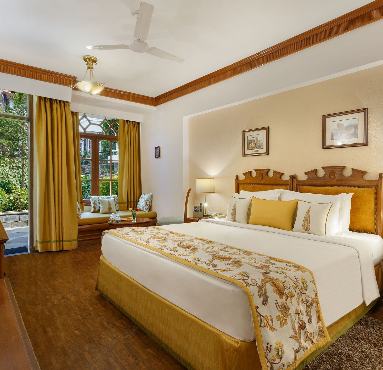 An image of a garden facing room in the naini retreat, nainital, with a king-size bed, wooden furniture, and a window. The room also features a ceiling fan, a TV and wooden flooring.