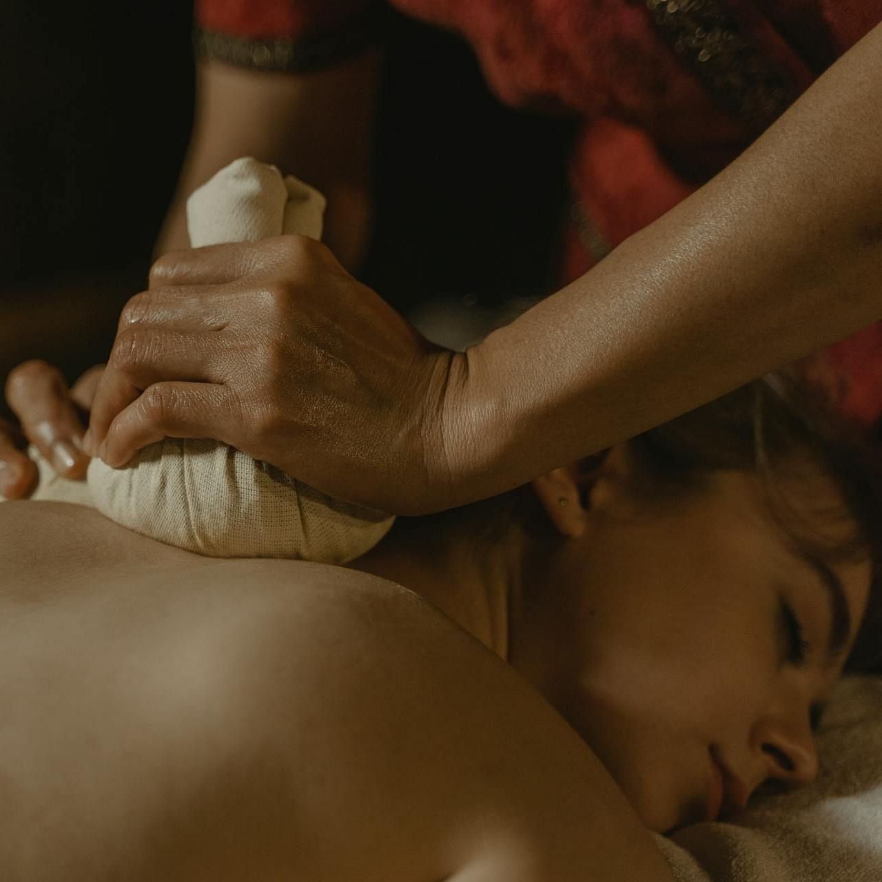 A lady laying in a spa table and getting a back massage with a rice sack