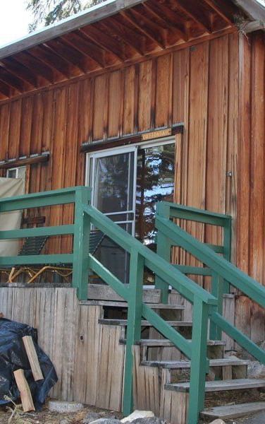 A rustic cabin with wood siding and a slanted roof nestled among tall trees. - Kit Carson Lodge & Restaurant 