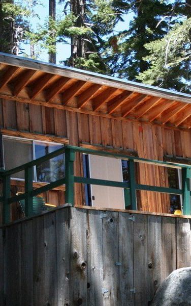 A rustic cabin with a trimmed deck nestled among tall trees, featuring a slanted roof. - Kit Carson Lodge