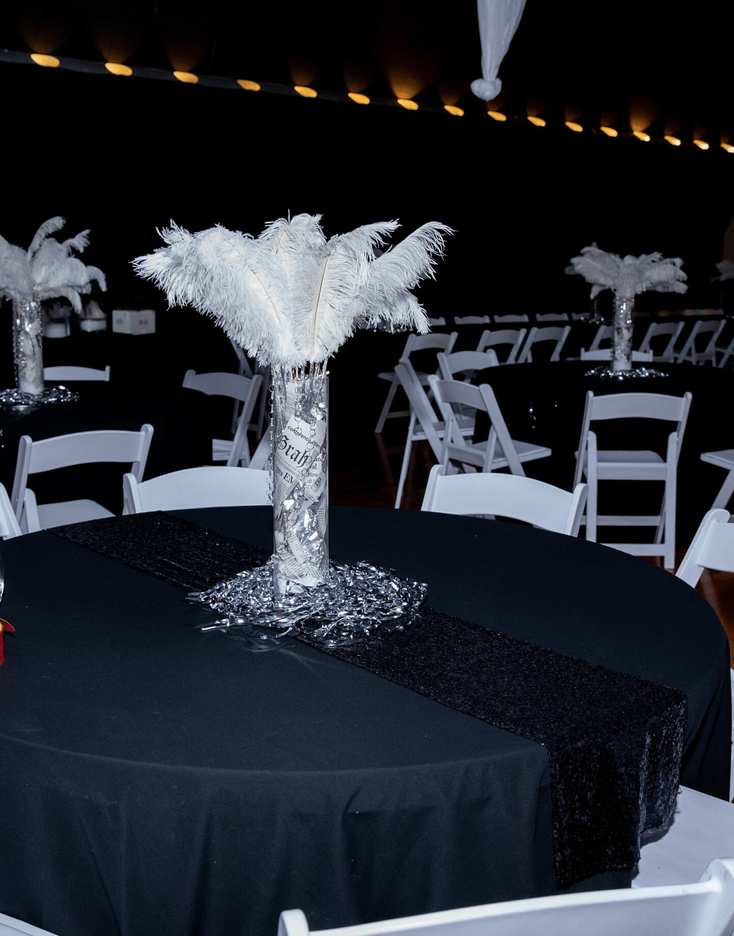 a round table featuring a cylindrical vase holding white feathers surround by white folding chairs at the Tin Can Theater - Historic Tapoco Lodge