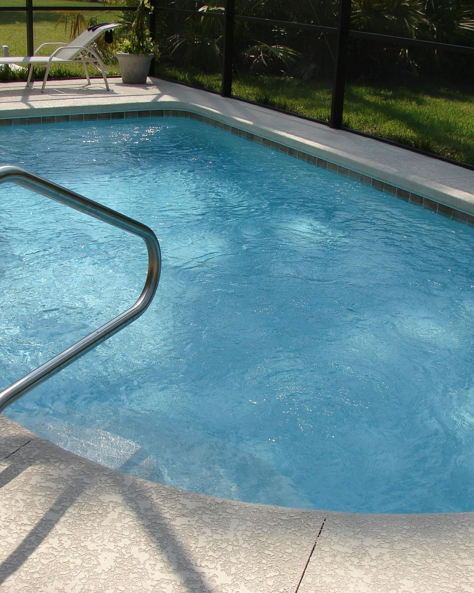 A rectangular swimming pool with clear blue water is surrounded by paving and greenery.