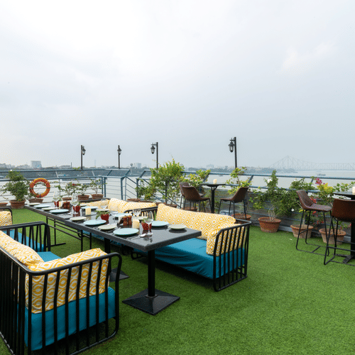  An outdoor dining setup on a rooftop garden overlooking a bridge and river during daylight - Polo Floatel